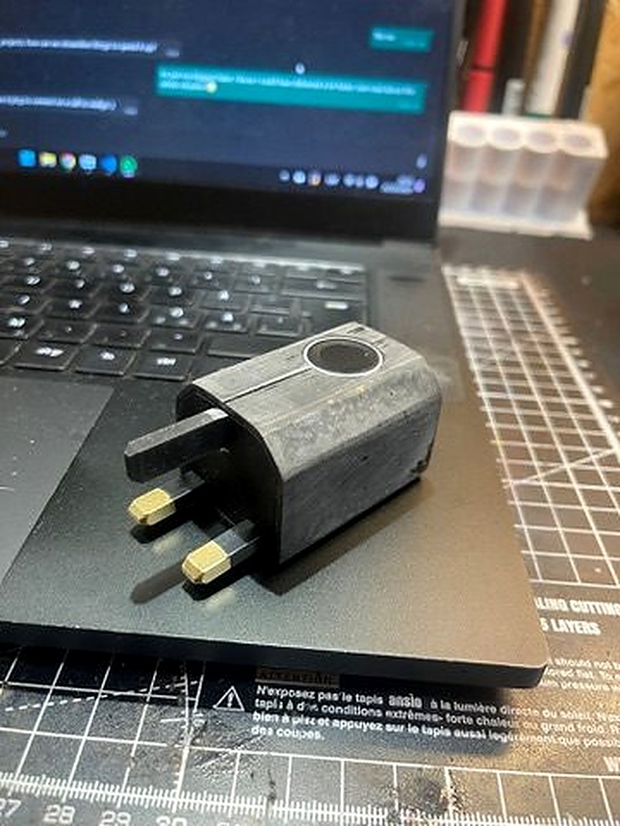 Dark resin 3D-printed Charlie Charger prototype with UK plug pins, on workbench