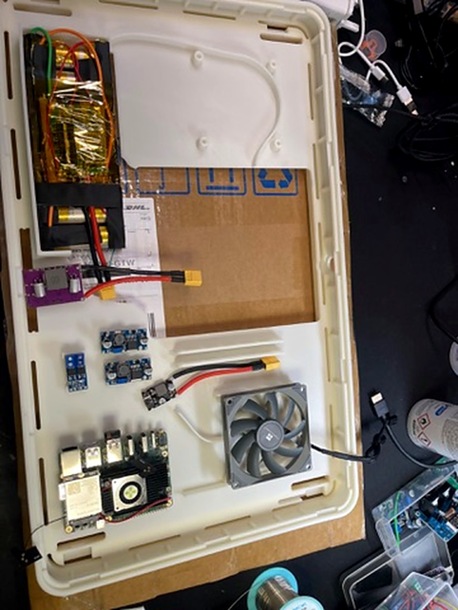 Early Genboard prototype showing Radxa SBC, fan, power boards, and LiPo cells laid out in white case frame